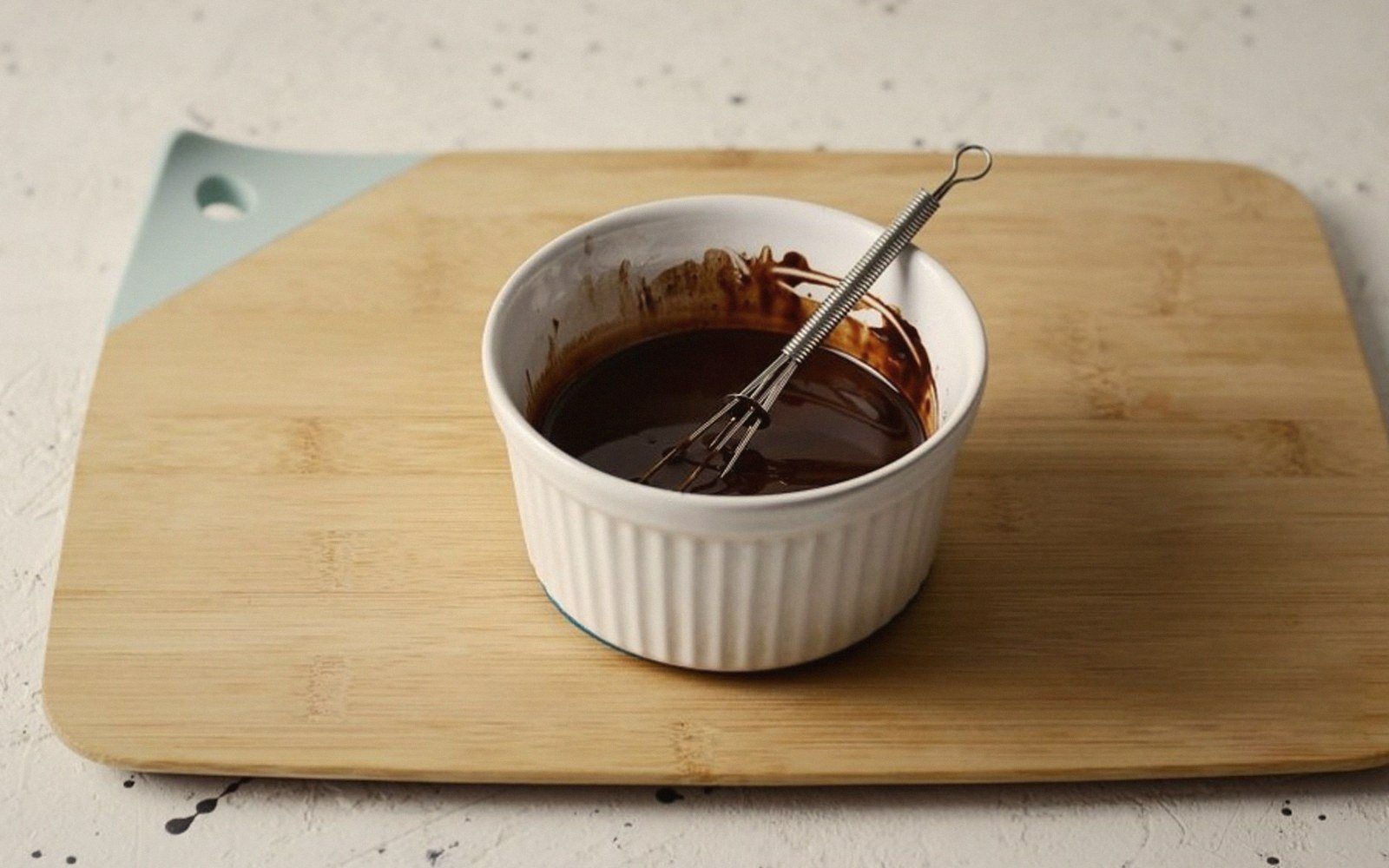 Melted chocolate with a small whisk in a white ramekin on a wooden board