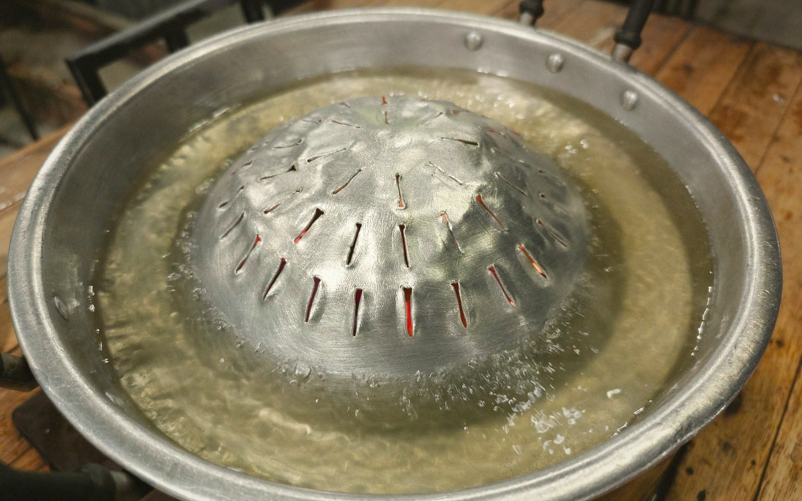 A slotted metal dome sits in a large tray filled with cloudy starch-washed water