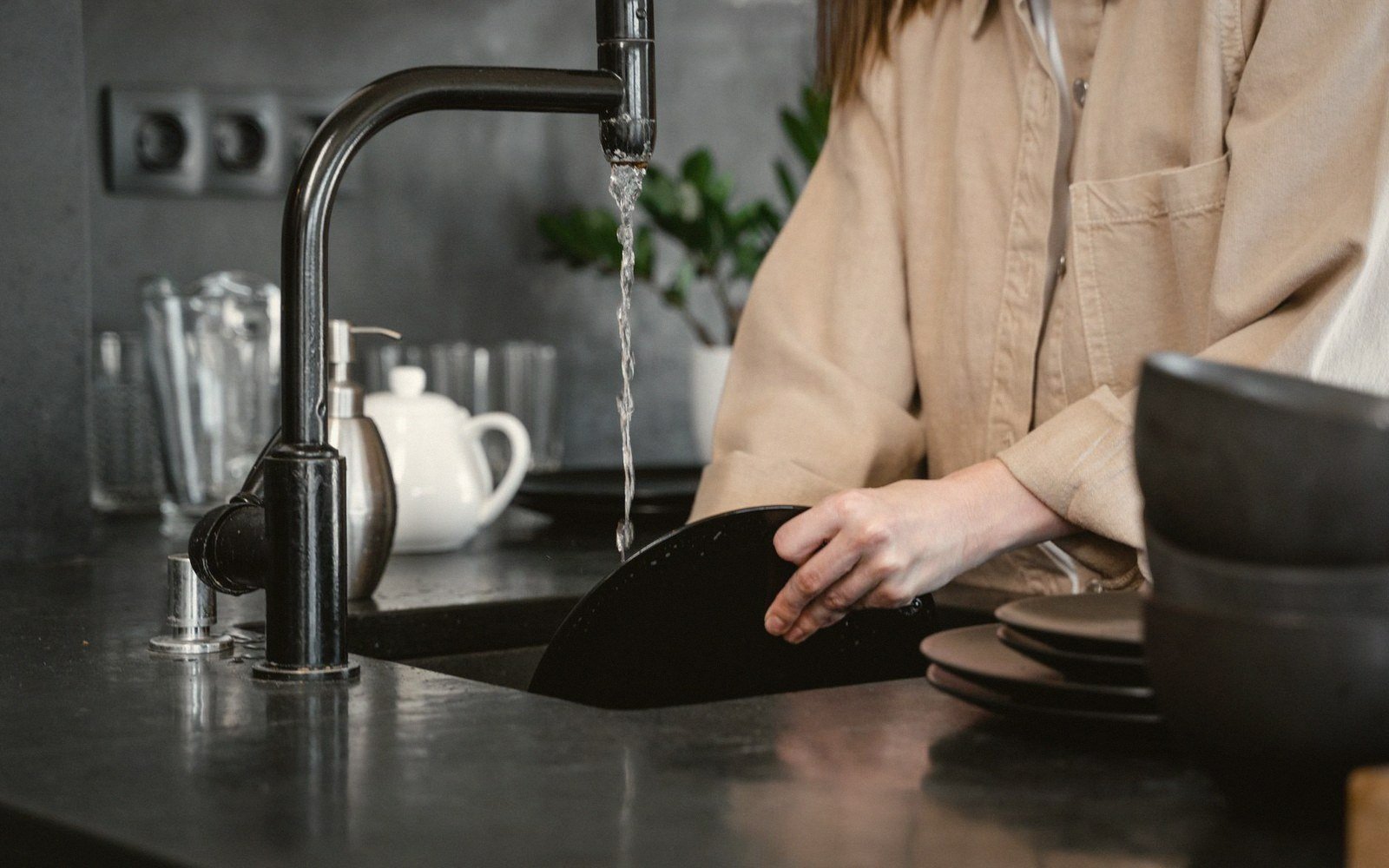 Person rinsing black plates under running water at a kitchen sink